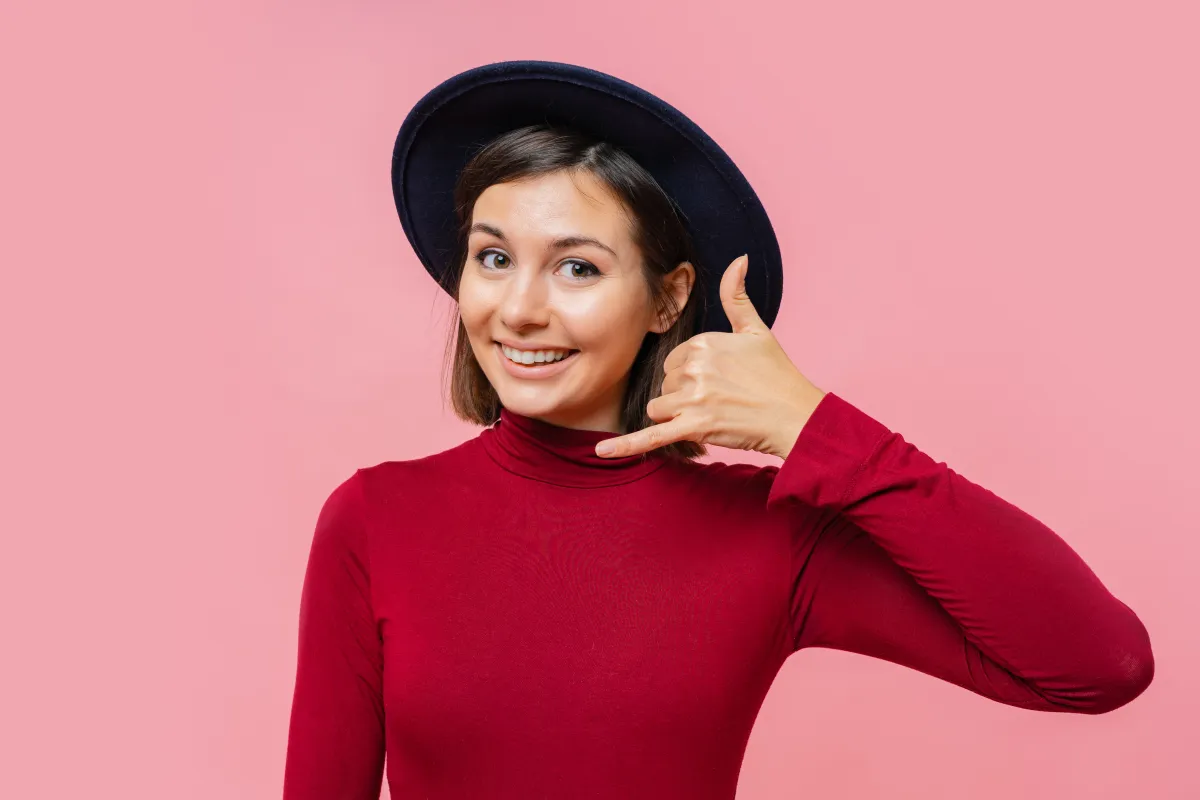 Leende person med hatt som gör en "ring oss"-gest med handen.